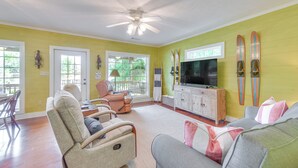 A living room with yellow walls, a ceiling fan, a television, and skis on the wall. - Private Dock + Porch: Lakefront Retreat in Cobb! (Cobb)
