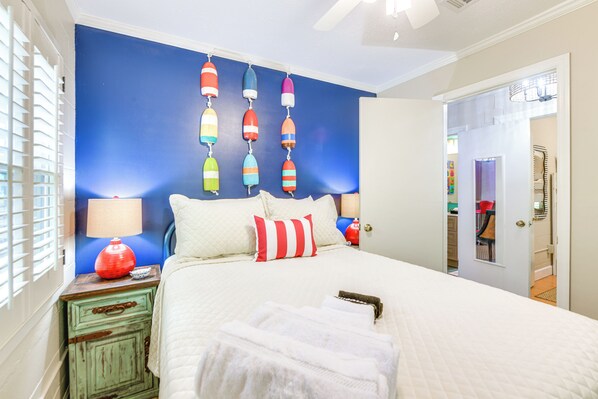 A bedroom with a bed, pillows, a nightstand, a lamp, and a wall with colorful hanging decorations. - Private Dock + Porch: Lakefront Retreat in Cobb! (Cobb)