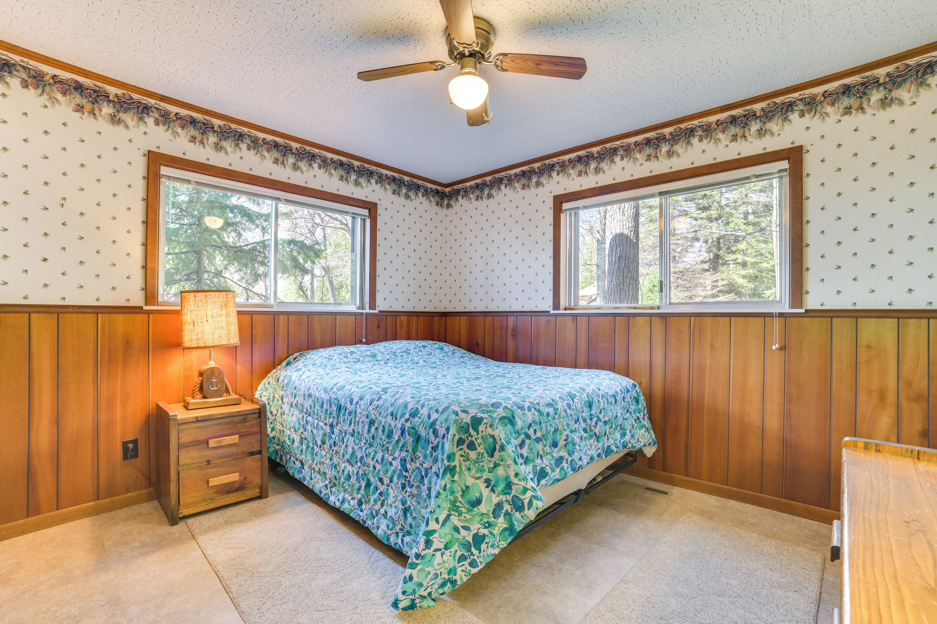 A bedroom with a bed, a nightstand, a ceiling fan, and two windows.