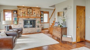 A living room with a brick fireplace, leather sofas, a wooden staircase, and a wooden door. - Tennis Court & Deck: Pet-friendly Charles City Gem (Charles City)