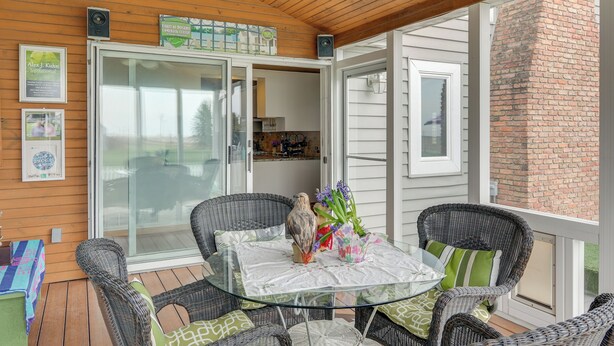A covered patio with wicker furniture, a glass table, and a view of the kitchen through glass doors. - Tennis Court & Deck: Pet-friendly Charles City Gem (Charles City)