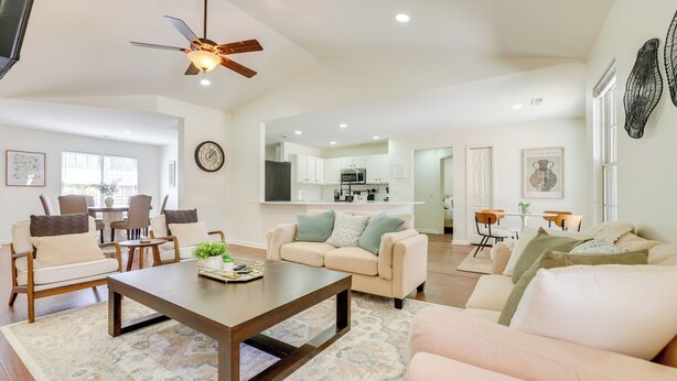 A spacious living room with a sofa, coffee table, and chairs. A kitchen is visible in the background. - Mini Putting Green & Fire Pit: Simpsonville Gem (Simpsonville)