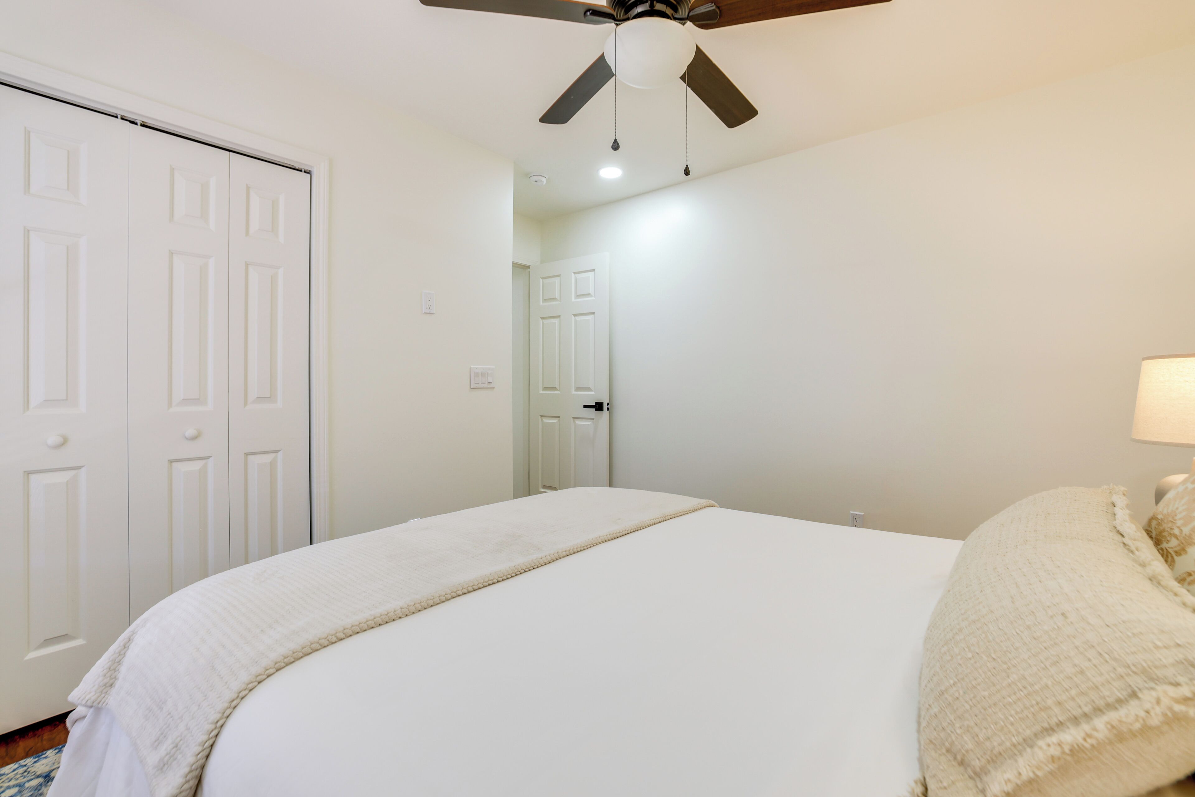 A bedroom with a bed, a ceiling fan, and a door.