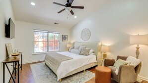 A bedroom with a bed, a ceiling fan, a window, a bedside table, a chair, and a lamp. - Mini Putting Green & Fire Pit: Simpsonville Gem (Simpsonville)