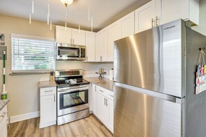 A modern kitchen with stainless steel appliances, white cabinetry, and a wooden floor.