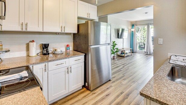 A modern kitchen with white cabinets, stainless steel appliances, and a wooden floor.
