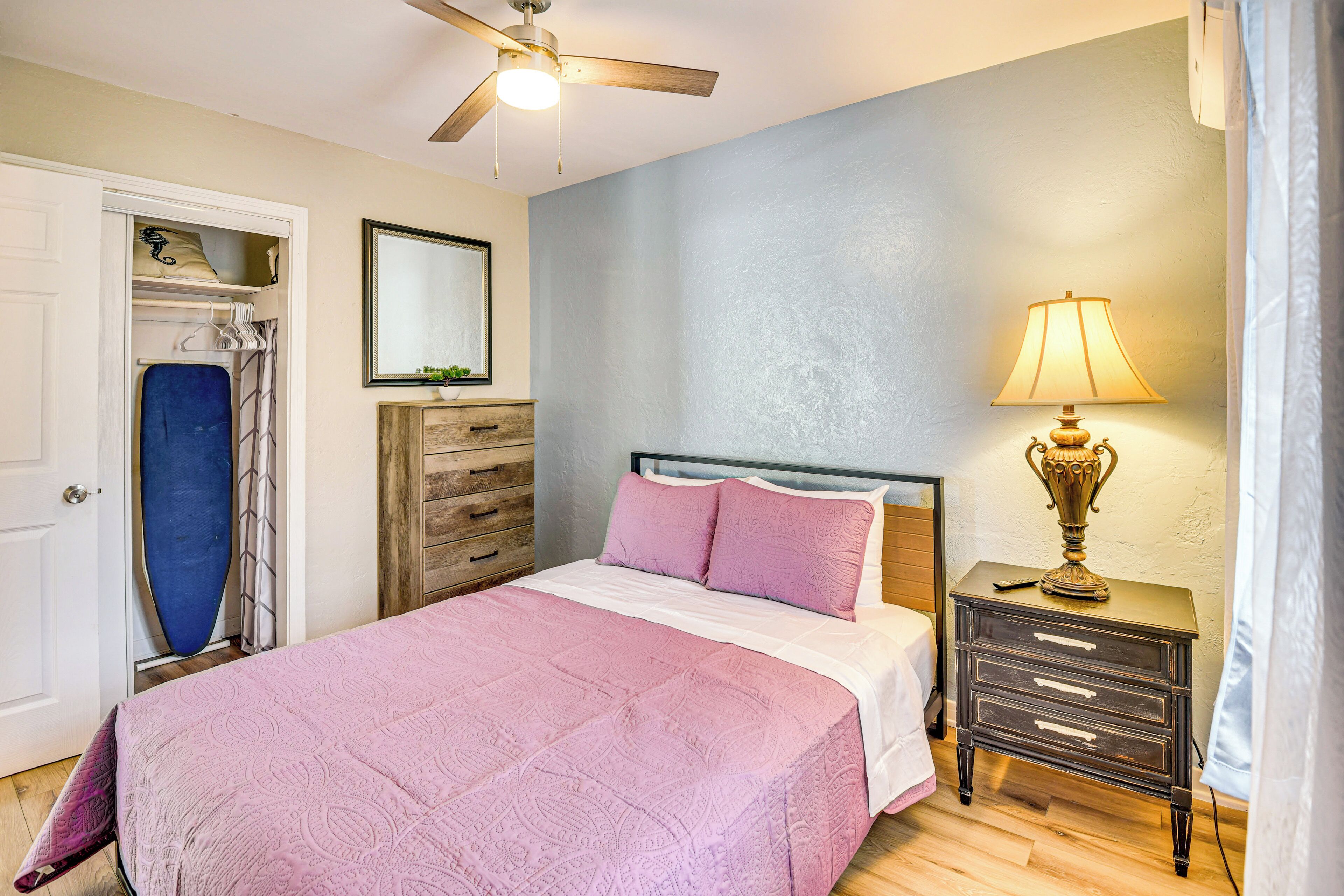 A bedroom with a bed, a nightstand with a lamp, a dresser, a ceiling fan, and a door with a shower curtain.