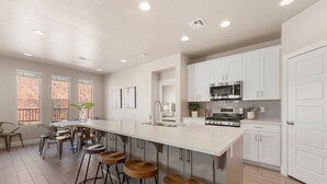 A modern kitchen with white cabinets, a stainless steel stove, and a long island with stools. - Desert Serenity: Community Pool + Hot Tub, Ping Pong Table! (Washington)