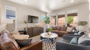 A living room with a large window, a flat-screen TV, a coffee table, and a sofa. - Desert Serenity: Community Pool + Hot Tub, Ping Pong Table! (Washington)