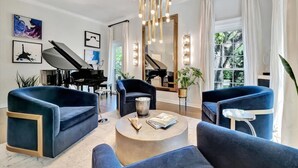 A modern living room with a piano, blue sofas, a coffee table, and a large mirror. - The Royale 2B 4B Luxury Garden Pool Yoga Room (Tampa)