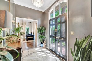 A modern interior with a large black door, a chandelier, and various plants. - The Royale 2B 4B Luxury Garden Pool Yoga Room (Tampa)