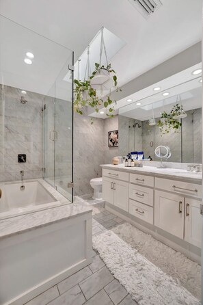 A modern bathroom with a glass-enclosed shower, a large bathtub, a white vanity with a mirror, and a marble floor. - The Royale 2B 4B Luxury Garden Pool Yoga Room (Tampa)