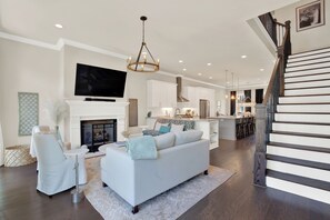 A modern living room with a white sofa, a fireplace, and a staircase leading to an upper level.