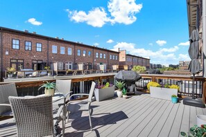 A rooftop deck with wicker chairs, planters, and a barbecue grill.