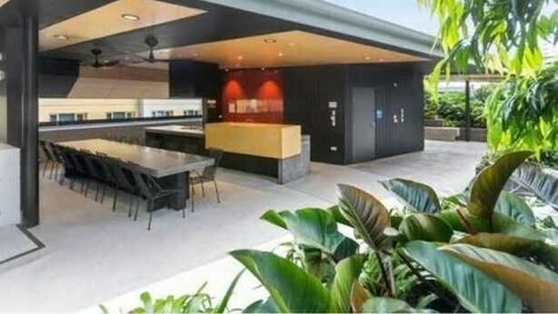 A modern outdoor kitchen with a dining area, large windows, and potted plants.