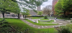 Um pátio bem cuidado com um jardim circular, caminhos pavimentados e um edifício grande ao fundo.
