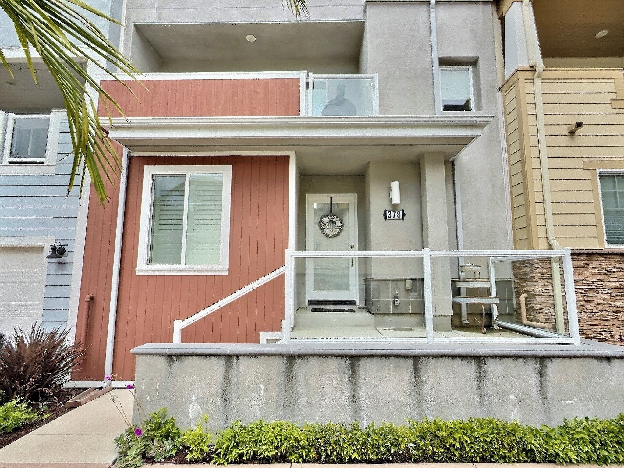 A two-story residential building with a concrete front porch, a mailbox, and a door with a wreath.