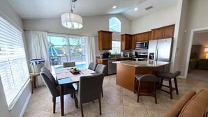Una cocina moderna con una isla central, comedor con sillas y vistas a una piscina.