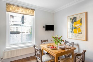 A dining area with a wooden table, chairs, a bowl of strawberries, a vase of tulips, and a framed artwork on the wall. - Beautiful 3-Bdr Chelsea Home with Garden patio – Steps from King’s Rd (London)