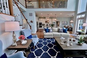 A spacious living room with a high ceiling, a staircase, and a kitchen in the background. - New Listing * 7 BR Coastal Club Resort Style Luxur (Lewes)