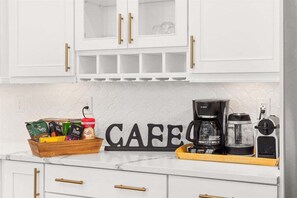 A kitchen with white cabinets, a coffee maker, a coffee grinder, and a coffee bean container.