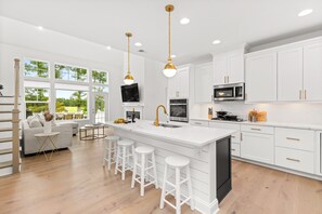 A modern kitchen with white cabinetry, a large island with stools, a built-in oven, and a TV mounted above the island.