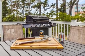 A barbecue grill, a can of beer, and grilling tools on a wooden table.