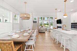 A modern kitchen with white cabinetry, a wooden dining table, and bar stools.