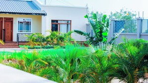 A modern house with a flat roof, a front porch, and a well-maintained garden with various plants.