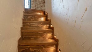A wooden staircase with a white textured wall on one side and a brick wall on the other.