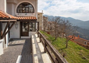 Un bâtiment avec un toit en tuiles, un balcon doté d’une balustrade en bois et une vue sur les montagnes.