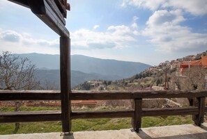 Un balcon en bois offrant une vue sur un village perché sur une colline et sur les montagnes.