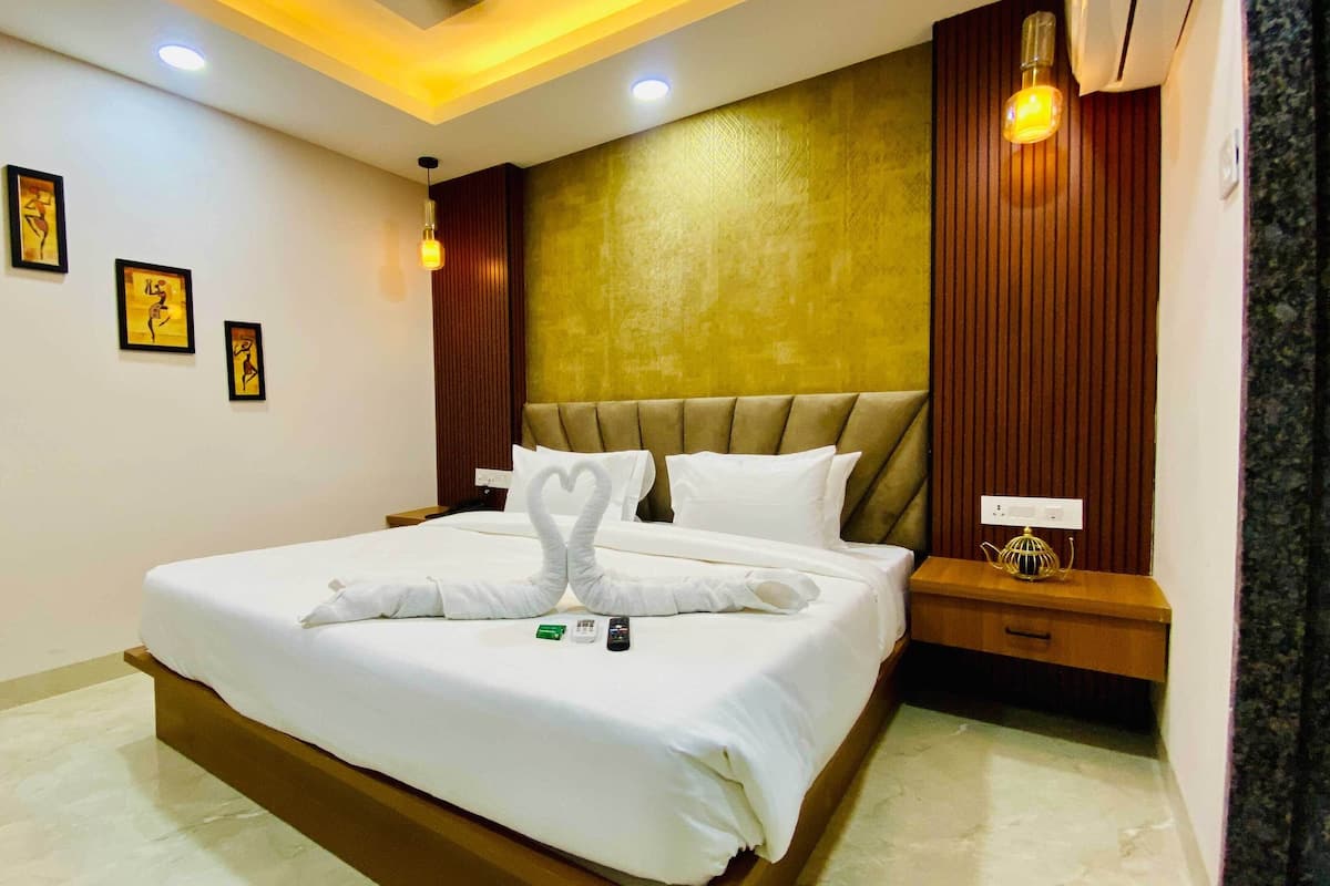 A hotel room with a large bed, a wooden headboard, a bedside table with a lamp, and framed artwork on the wall.