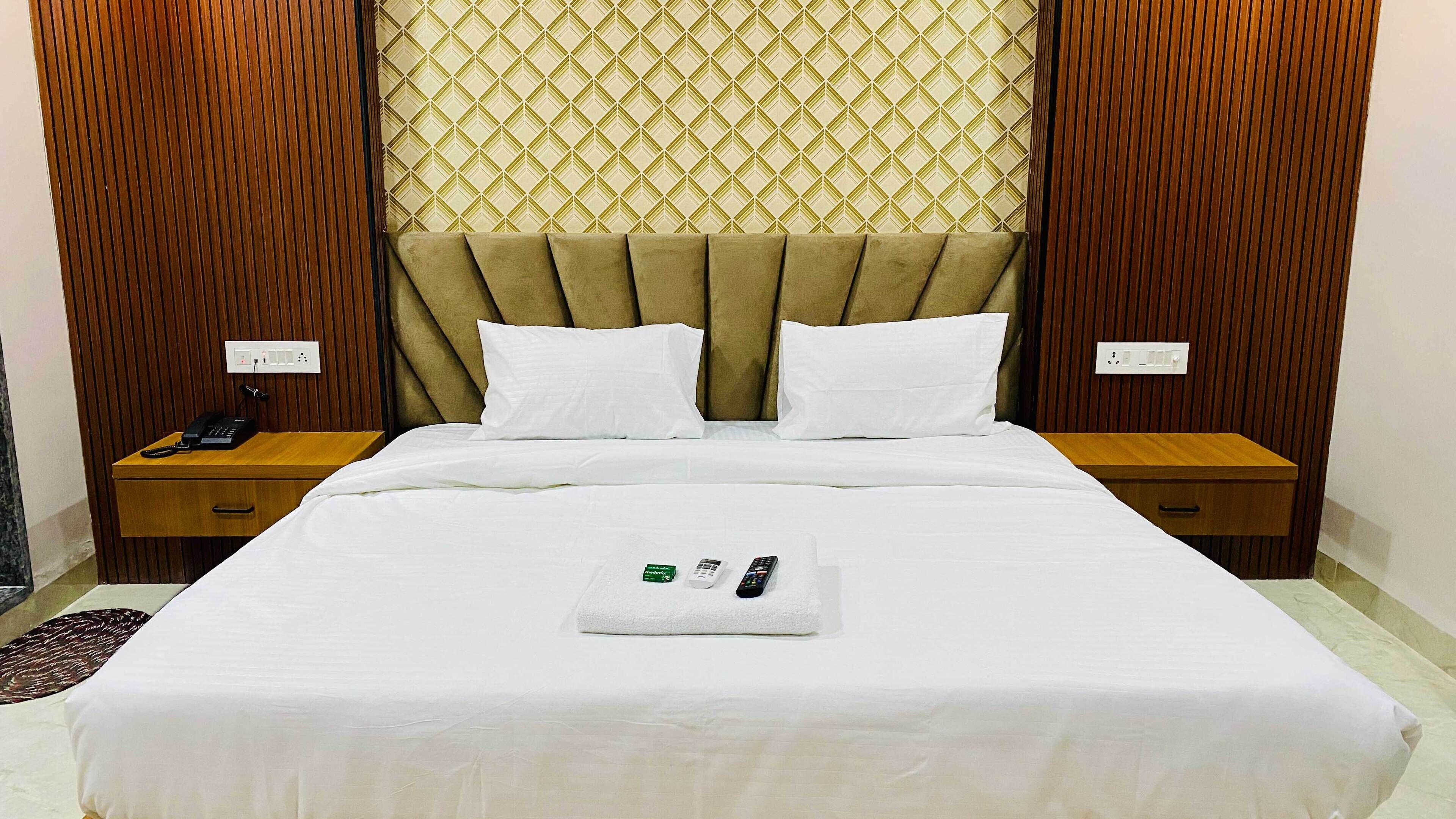 Una habitación de hotel con una cama grande, dos almohadas blancas, una mesita de noche de madera con un teléfono y un papel tapiz estampado.