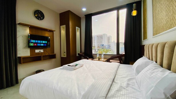 A hotel room with a large bed, a TV mounted on the wall, a window with a city view, and a small table with a chair. - Hotel Friendship Inn (Indore)