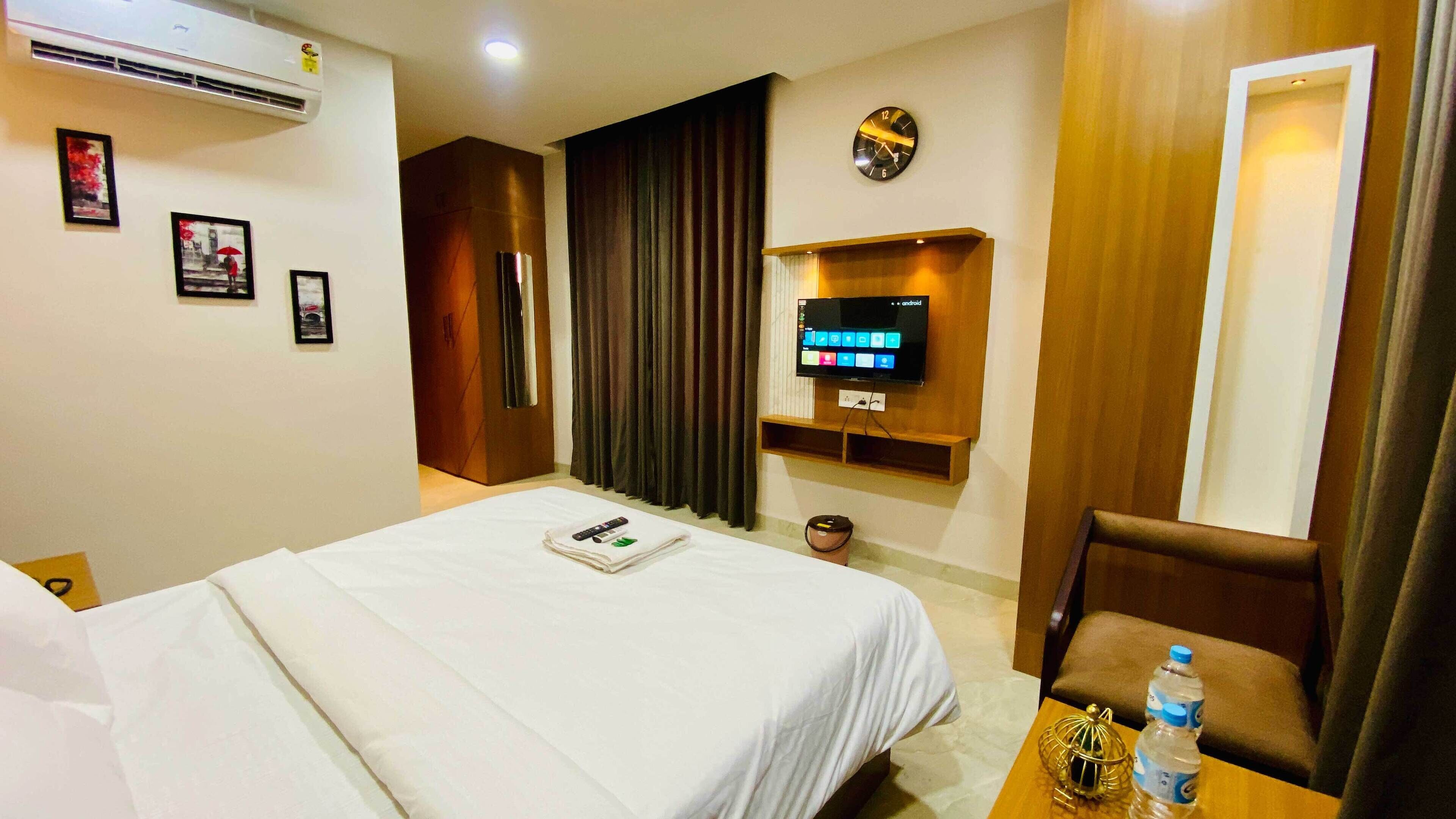 Una habitación de hotel con cama, televisión montada en la pared, escritorio con silla y una botella de agua sobre la mesa.