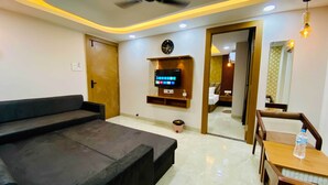 A modern living room with a sofa, a TV mounted on the wall, a wooden door, and a dining area with a table and chairs. - Hotel Friendship Inn (Indore)