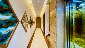 A hallway with a marble floor, framed artwork on the walls, and a glass door with patterned curtains. - Hotel Friendship Inn (Indore)