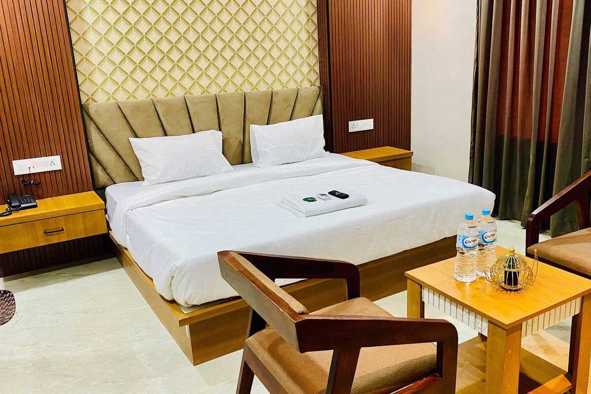 A hotel room with a bed, two wooden nightstands, a bedside table with a lamp, a small wooden table with two chairs, and a window with curtains.