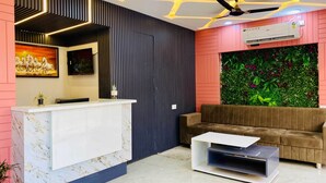 A reception area with a marble reception desk, a brown sofa, a small white coffee table, a ceiling fan, and a wall-mounted air conditioner. - Hotel Friendship Inn (Indore)