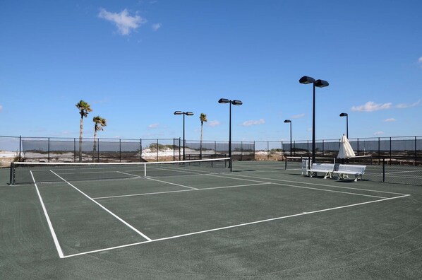 Una cancha de tenis con red, bancos y farolas.