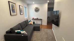 A modern living room with a sectional sofa, a flat-screen TV, and a decorative clock on the wall.
