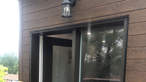 A modern building with a sliding glass door entrance, a wooden deck, and a metal railing.