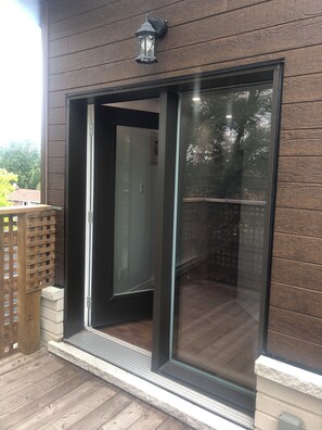 A modern building with a sliding glass door entrance, a wooden deck, and a metal railing.