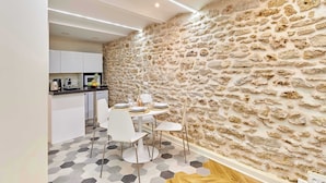 Une cuisine moderne avec des meubles blancs, un mur en pierre et un coin repas comprenant des chaises blanches et une table ronde.