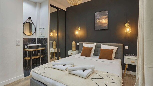 A modern bedroom with a bed, bedside tables, a mirror, and a wall-mounted artwork.