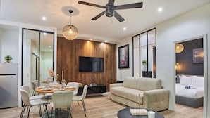A modern living room with a dining area, a sofa, a TV mounted on the wall, and a ceiling fan.