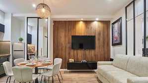 A modern living room with a dining area, a flat-screen TV mounted on a wooden wall, a sofa, and a dining table set for four.