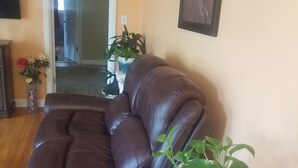 A brown leather sectional sofa in a living room with a wooden floor, a white column with a plant, and a door leading to another room.