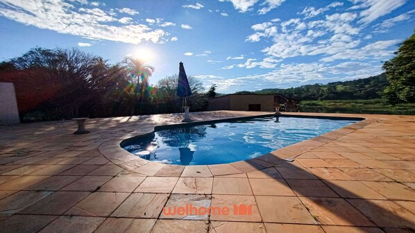 En swimmingpool med buet kant, omgivet af en flisbelagt terrasse.